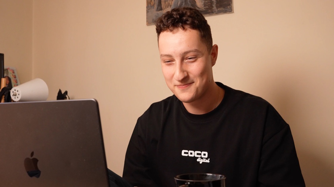 Anthony Lococo, founder of COCO Creators, smiling at his laptop in a COCO Digital t-shirt